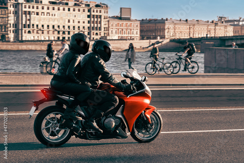 A man and a woman ride together on a sports motorcycle along the embankment. Motorcyclists travel around the city during the day on a red sports bike.