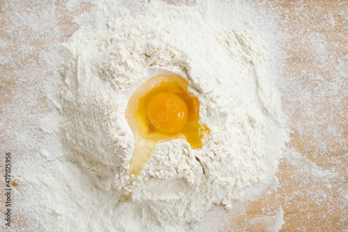 Flatlay of pile of sifted flour with raw egg on top ready for preparation of homemade dough and pastry