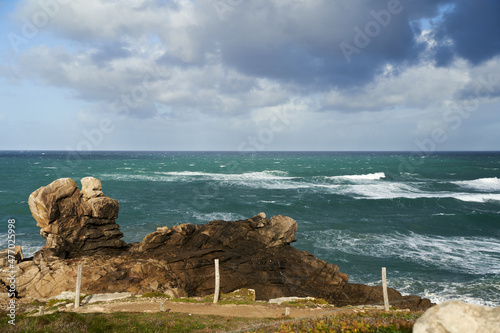 Rocks at the water's edge from the beach. Cloudy sky in sunlight. Well known surf spot in La Torche in Brittany near Plomeur. photo