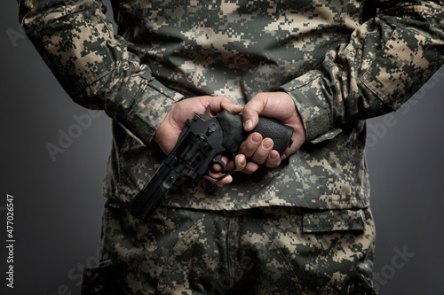 A man in an American camouflage uniform with a pistol in his hand behind his back. The readiness for hostilities and the turbulent political environment. Gray background. photo