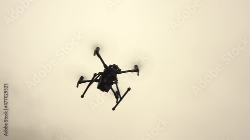 An unmanned helicopter with a video camera hovers in the sky. Modern military drone.