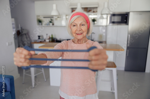 Foto Cheerful senior woman exercising with rubber expander to strengthen her arm musc