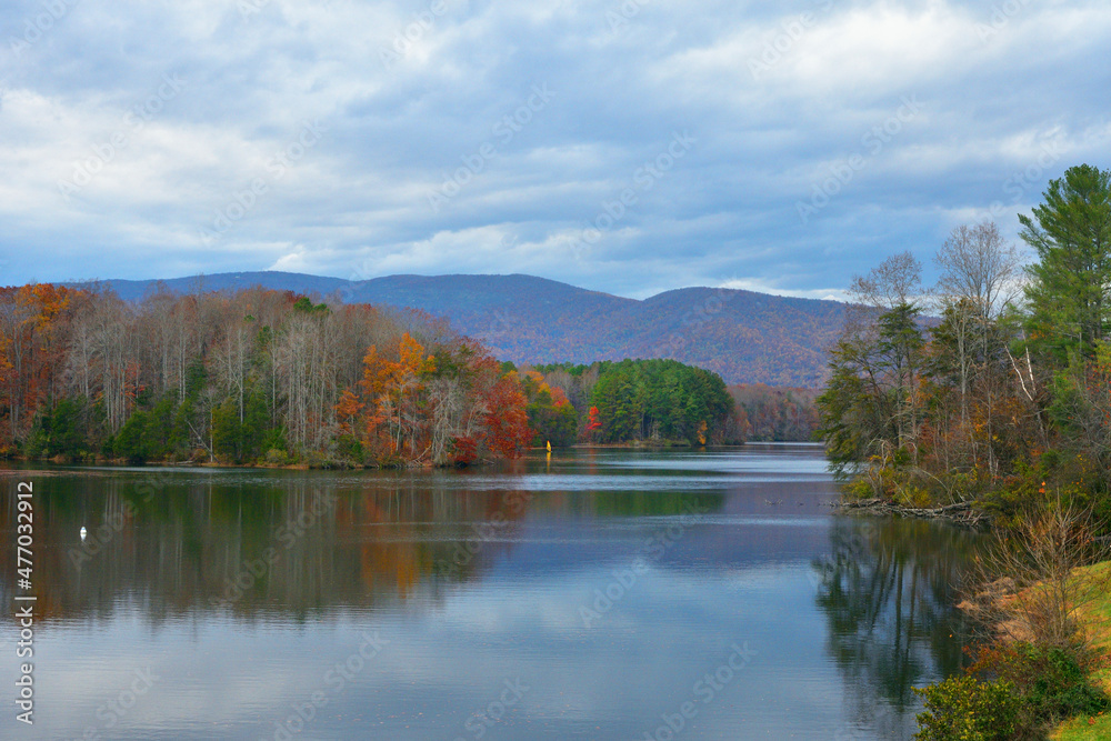 A windsurfer navigates on a pristine mountain lake with colorful clouds and autumnal colors in the trees. A windsurfer navigates on a pristine mountain lake with colorful clouds and autumnal colors in the trees.