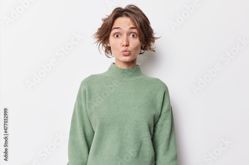Portrait of surprised brunette young woman with trendy hairstyle keeps lips folded wears casual jumper blows you kiss isolated over white background. Facial expressions and romantic mood concept © wayhome.studio 