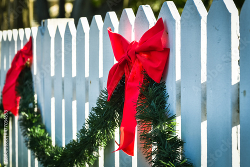 Christmas holiday outdoor decorations with red ribbon bows and green pine garland on white picket fence photo