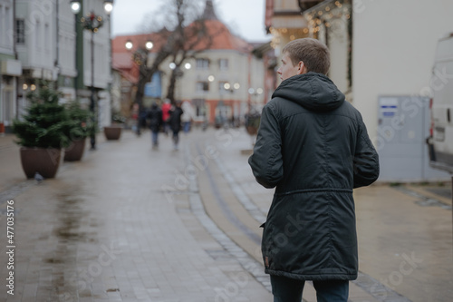 a young guy in a black jacket walks forward along a city street examines the sights