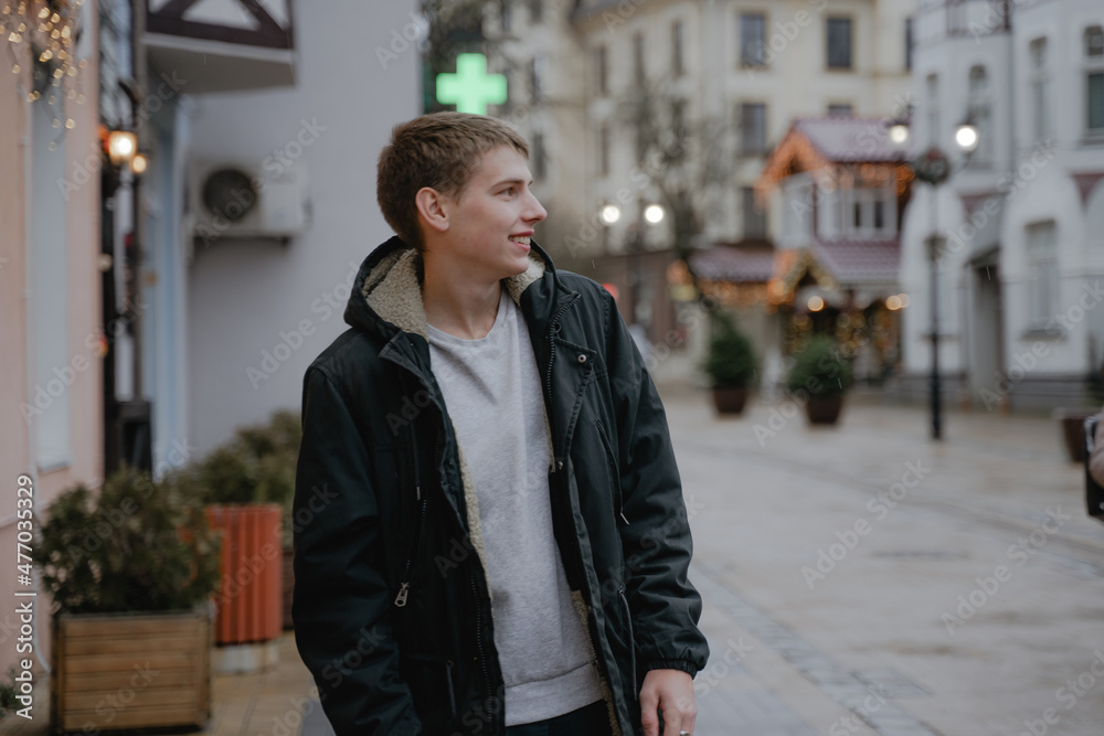 portrait of a smiling teenager in profile, in a black winter jacket on the city streets