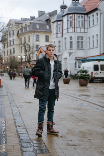 a teenager in a black jacket stands in the middle of the street looking at the camera