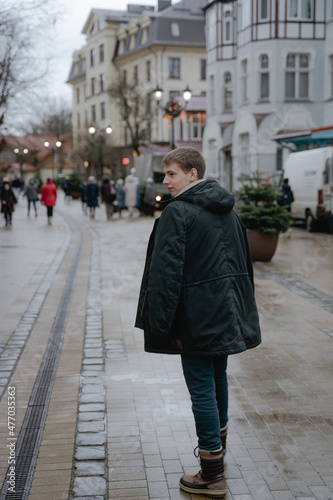 a young guy walks forward in a winter black jacket, slightly turned around and looked to the side