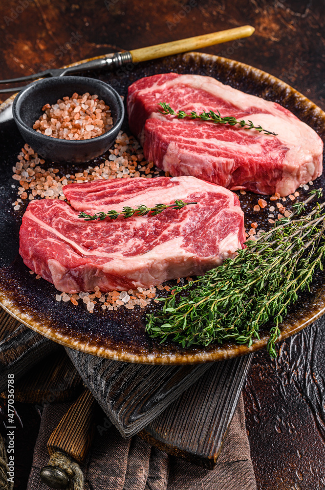 Chuck eye Roll beef steaks, raw meat  on a plate with thyme and herbs. Dark background. Top view