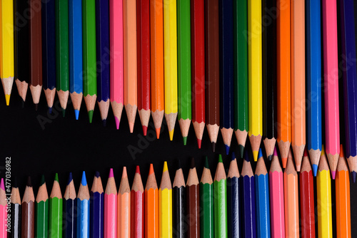 Close up of lots of wooden crayons of different colors facing each other to form an opening zipper against a black background