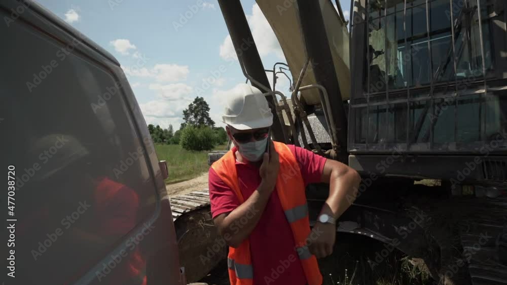 custom made wallpaper toronto digitalBuilder wearing face mask orange vest and white helmet talking by phone standing at construction site against heavy excavator outdoor
