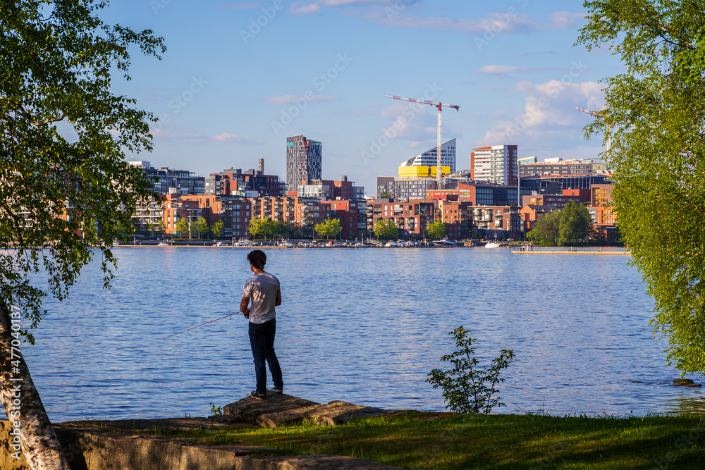 Man fishing at the Hatanpää arboretum, view of Tampere city over the lake Pyhäjärvi in Finland in the summer.