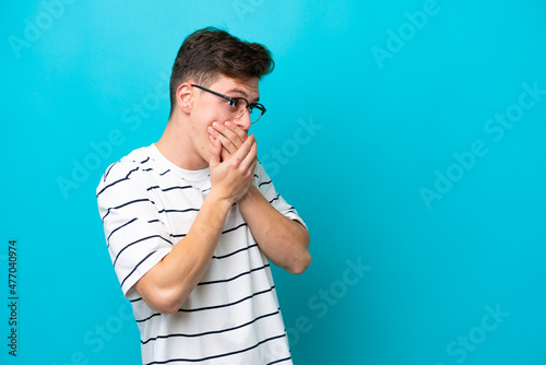 Young handsome Brazilian man isolated on blue background covering mouth and looking to the side