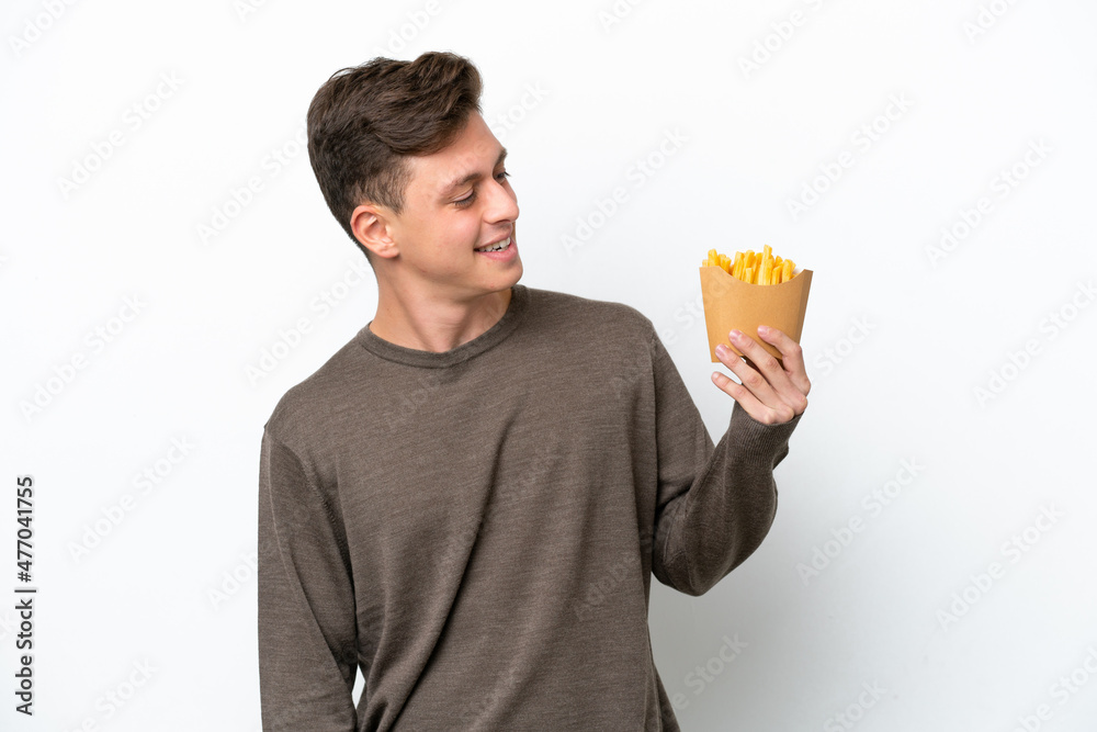 Young Brazilian man holding fried chips isolated on white background looking to the side and smiling Young Brazilian man holding fried chips isolated on white background looking to the side and smiling