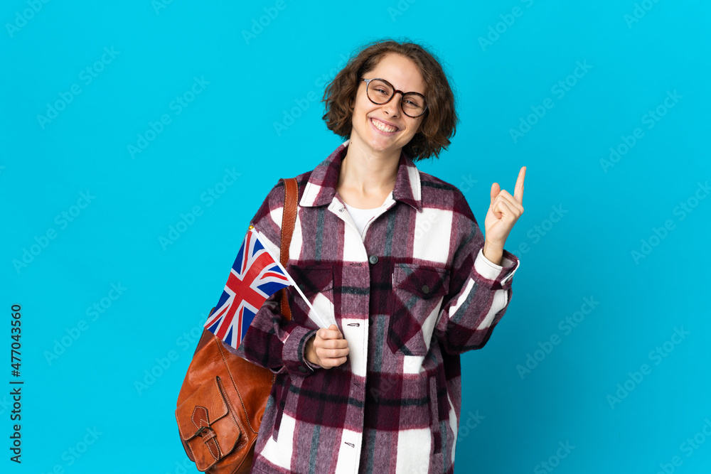 Young English woman holding an United Kingdom flag isolated on blue background showing and lifting a finger in sign of the best