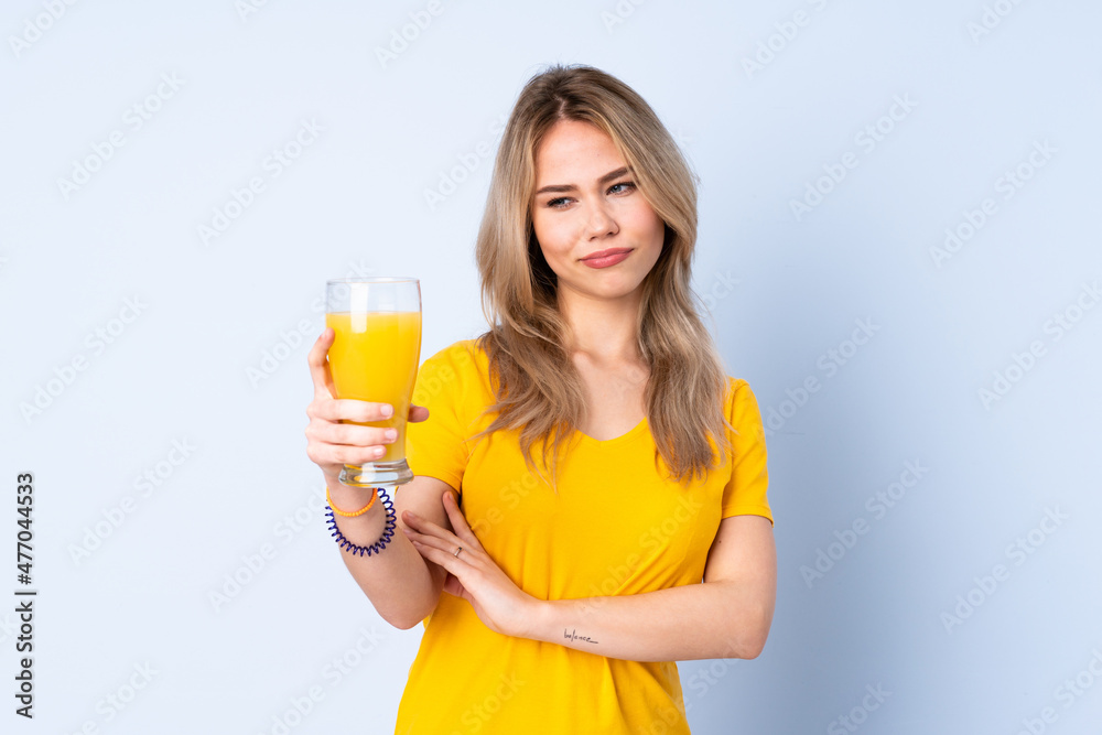 Teenager Russian girl holding an orange juice isolated on blue background with sad expression Teenager Russian girl holding an orange juice isolated on blue background with sad expression