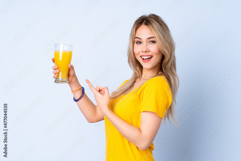 Teenager Russian girl holding an orange juice isolated on blue background and pointing it Teenager Russian girl holding an orange juice isolated on blue background and pointing it