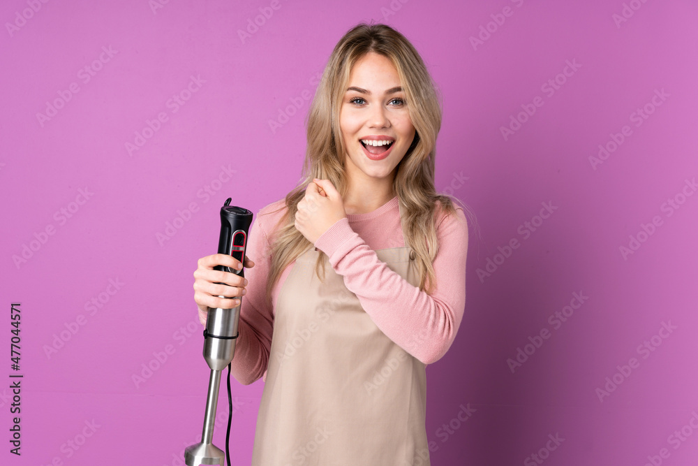 Teenager Russian girl using hand blender isolated on purple background celebrating a victory