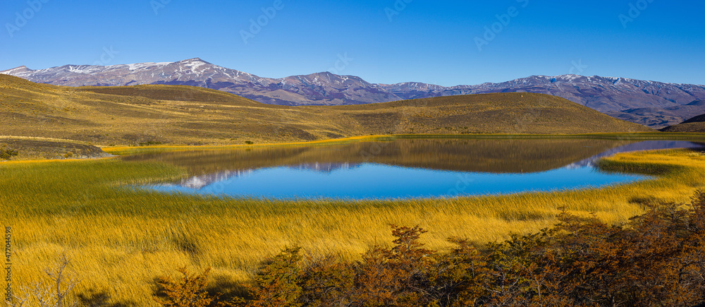 Panoramic view on an autumn landscape with mountains, rolling hills, and a lake under under clear blue sky in Patagonia, Chile