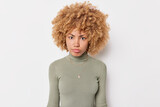 Portrait of serious young woman has strict angry expression focused at camera dressed in casual jumper poses against white background listens someone attentively analyzes received information