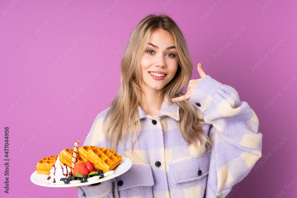 Teenager Russian girl holding waffles isolated on purple background making phone gesture. Call me back sign Teenager Russian girl holding waffles isolated on purple background making phone gesture. Call me back sign