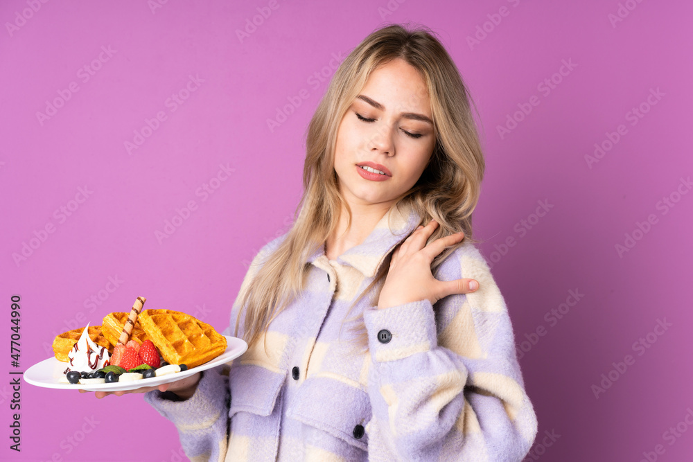 Teenager Russian girl holding waffles isolated on purple background suffering from pain in shoulder for having made an effort Teenager Russian girl holding waffles isolated on purple background suffering from pain in shoulder for having made an effort