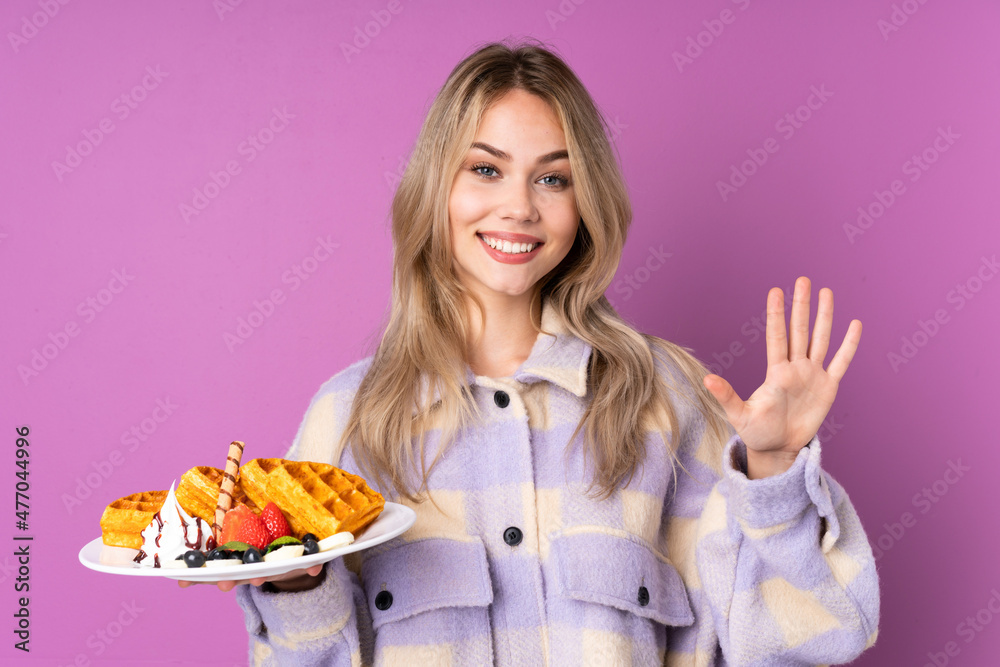 Teenager Russian girl holding waffles isolated on purple background counting five with fingers