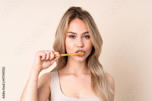 Teenager blonde girl brushing her teeth over isolated background