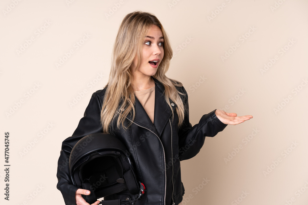 Russian girl with a motorcycle helmet isolated on beige background with surprise facial expression Russian girl with a motorcycle helmet isolated on beige background with surprise facial expression