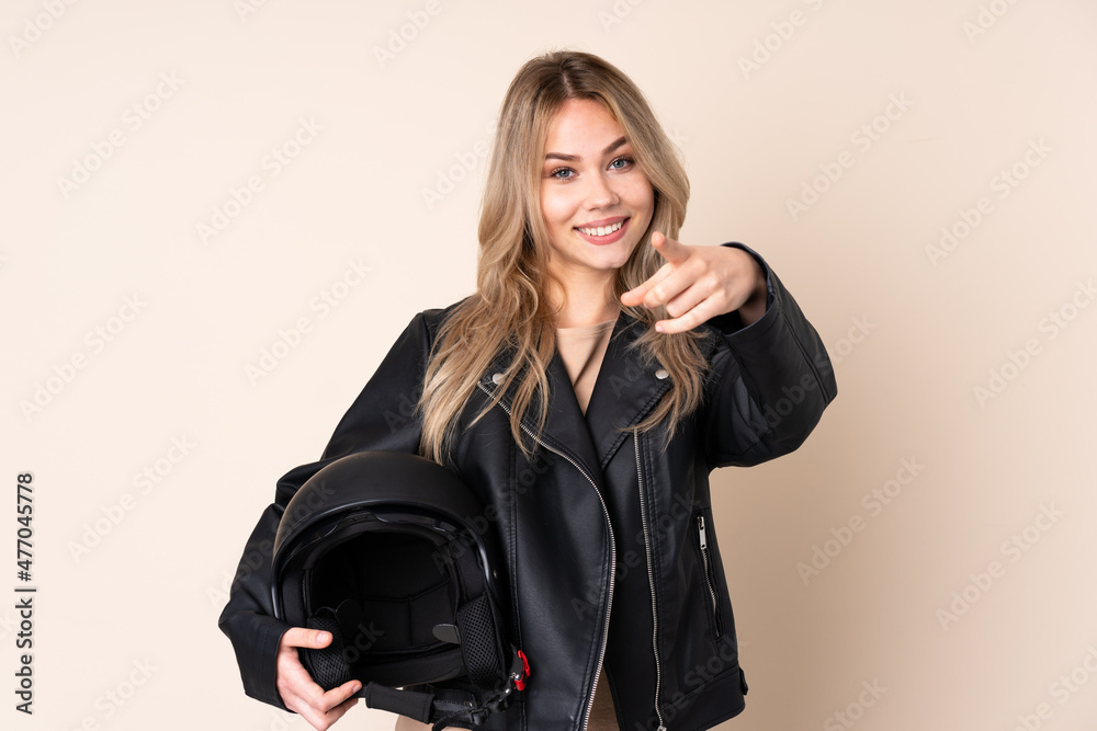 Russian girl with a motorcycle helmet isolated on beige background making phone gesture and pointing front Russian girl with a motorcycle helmet isolated on beige background making phone gesture and pointing front