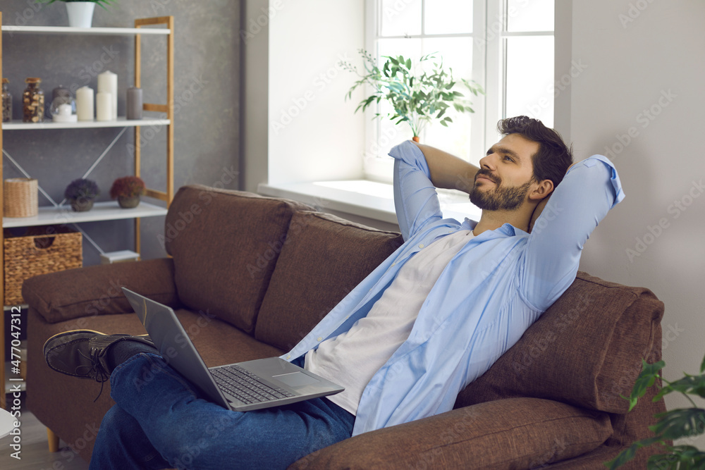 Happy young man takes break from work or studies. Relaxed handsome entrepreneur or college student lounging on comfortable sofa with laptop computer on lap, thinking hands behind head, daydreaming Happy young man takes break from work or studies. Relaxed handsome entrepreneur or college student lounging on comfortable sofa with laptop computer on lap, thinking hands behind head, daydreaming