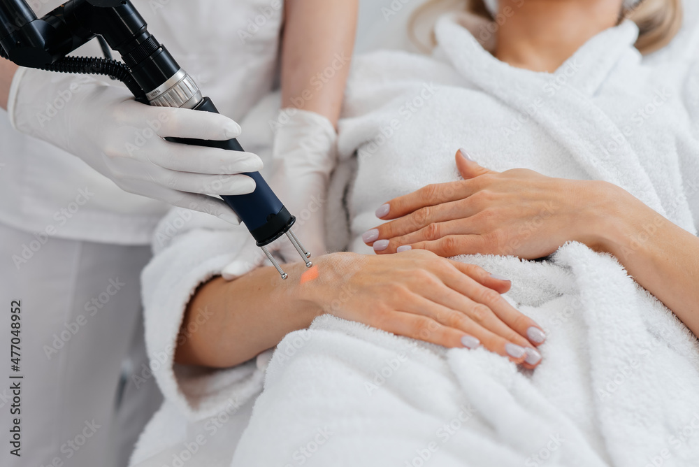 A young girl gets carbon peeling for the skin of her hands in a beauty salon. Laser pulses cleanse the skin. Hardware cosmetology. The process of photothermolysis, warming the skin. A young girl gets carbon peeling for the skin of her hands in a beauty salon. Laser pulses cleanse the skin. Hardware cosmetology. The process of photothermolysis, warming the skin.