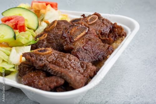 A view of a bento box, featuring Hawaiian style beef short ribs.