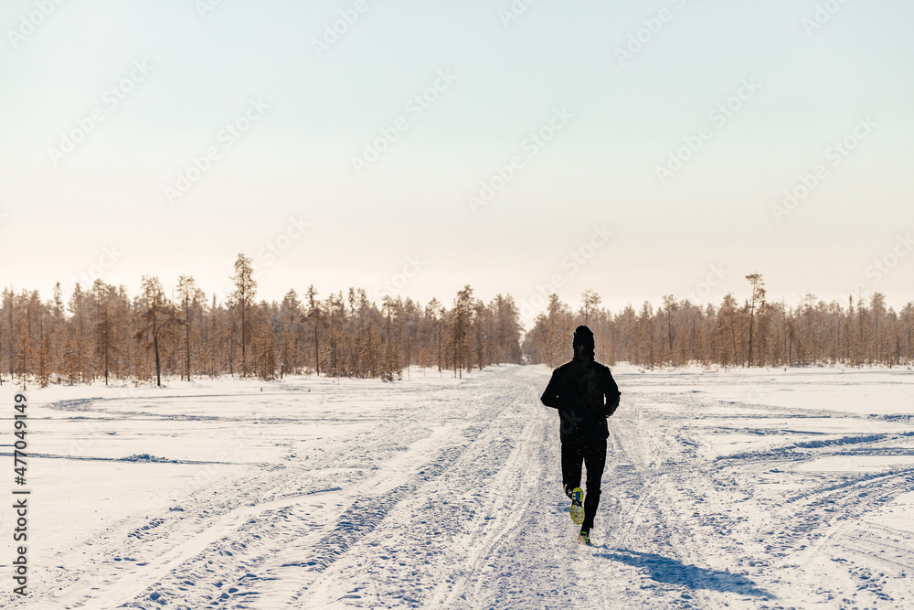  sporty man in sportswear running in a winter park, copy space. a runner trains outdoors, jogging in nature. concept of seasonal outdoor sports and cold hardening