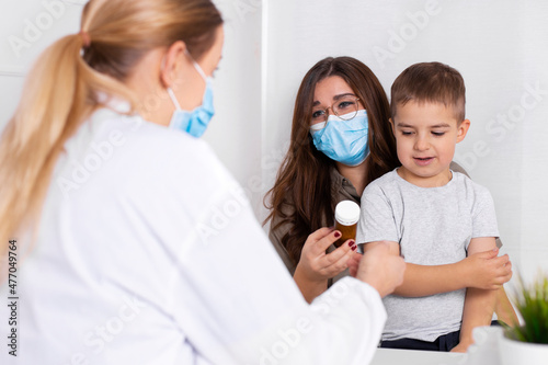 Young brunette woman with little boy having consultation at pediatrician office. Doctor, child and mother wearing facemasks during coronavirus and flu outbreak. Virus protection. Covid 19.