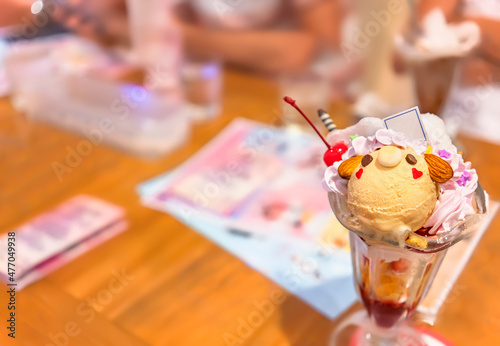 Japanese milk tea ice cream and almonds shaped as a cute bear character topped with sweet whipped cream and cherries in a glassware full of corn flakes against a blurry background.
