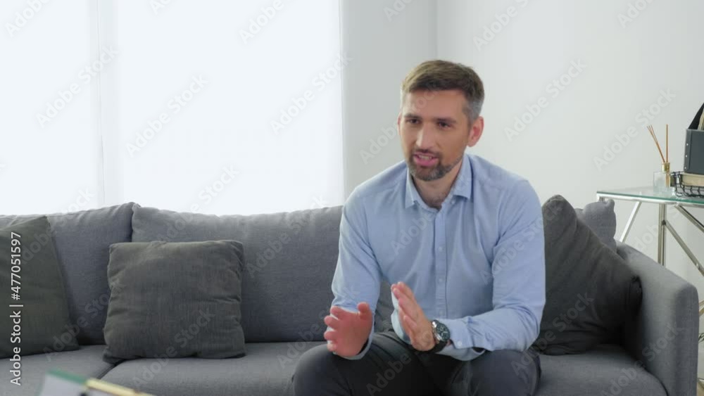 Camera zoom out smiling adult man patient with mental health problems sitting on couch talking to therapist. Woman psychologist with clipboard listen client at psychotherapy session in clinic office Camera zoom out smiling adult man patient with mental health problems sitting on couch talking to therapist. Woman psychologist with clipboard listen client at psychotherapy session in clinic office