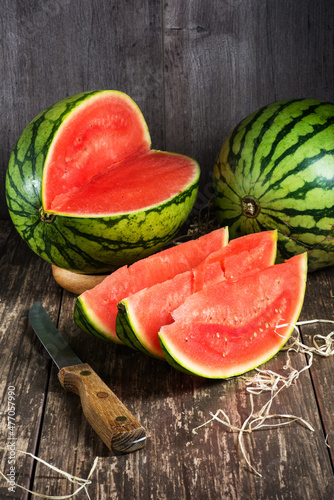A whole watermelon and Pieces of ripe watermelon, a knife with a wooden handle on a wooden background.