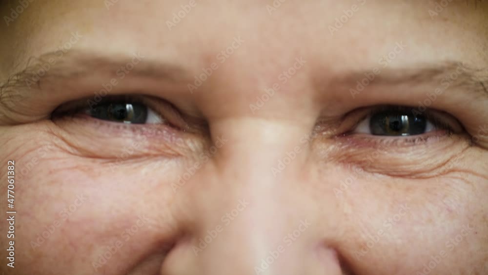 Face of happy middle aged woman smiling and laughing with blue eyes. Beautiful mature female portrait with wrinkles on attractive face looking at camera. Macro extreme close up, 4K.
