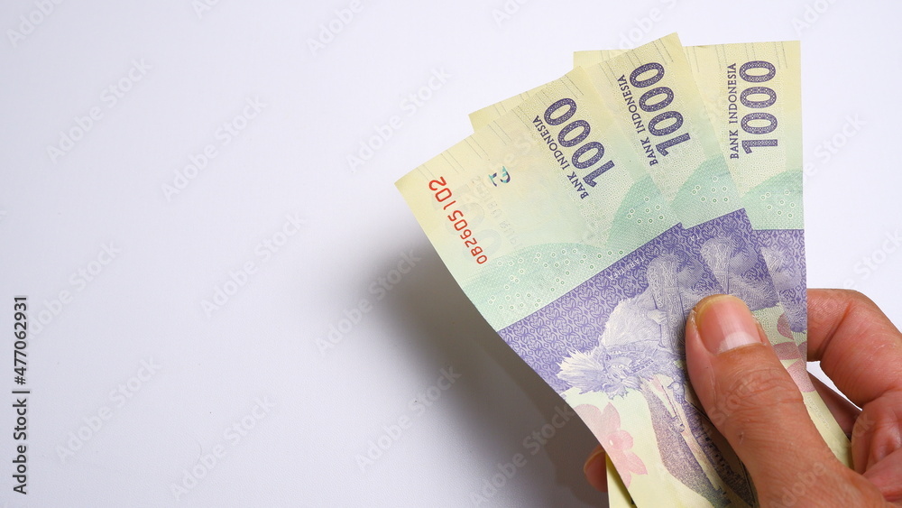 A man's hand is making a payment. Male hand showing Indonesian rupiah note. Indonesian Rupiah the official currency of Indonesia. Business and finance concept. Uang 1000 Rupiah. A man's hand is making a payment. Male hand showing Indonesian rupiah note. Indonesian Rupiah the official currency of Indonesia. Business and finance concept. Uang 1000 Rupiah.