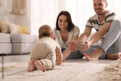 Happy parents watching their cute baby crawl on floor at home photo