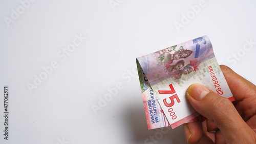 A man's hand is making a payment. Male hand showing Indonesian rupiah note. Indonesian Rupiah the official currency of Indonesia. Business and finance concept. Uang 75000 Rupiah. Bank Indonesia