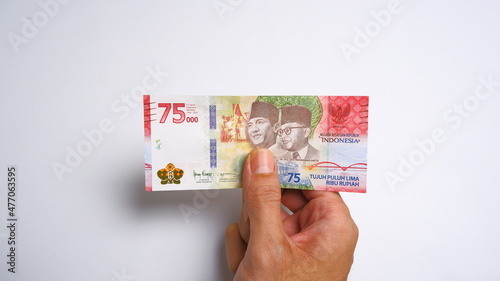 A man's hand is making a payment. Male hand showing Indonesian rupiah note. Indonesian Rupiah the official currency of Indonesia. Business and finance concept. Uang 75000 Rupiah. Bank Indonesia