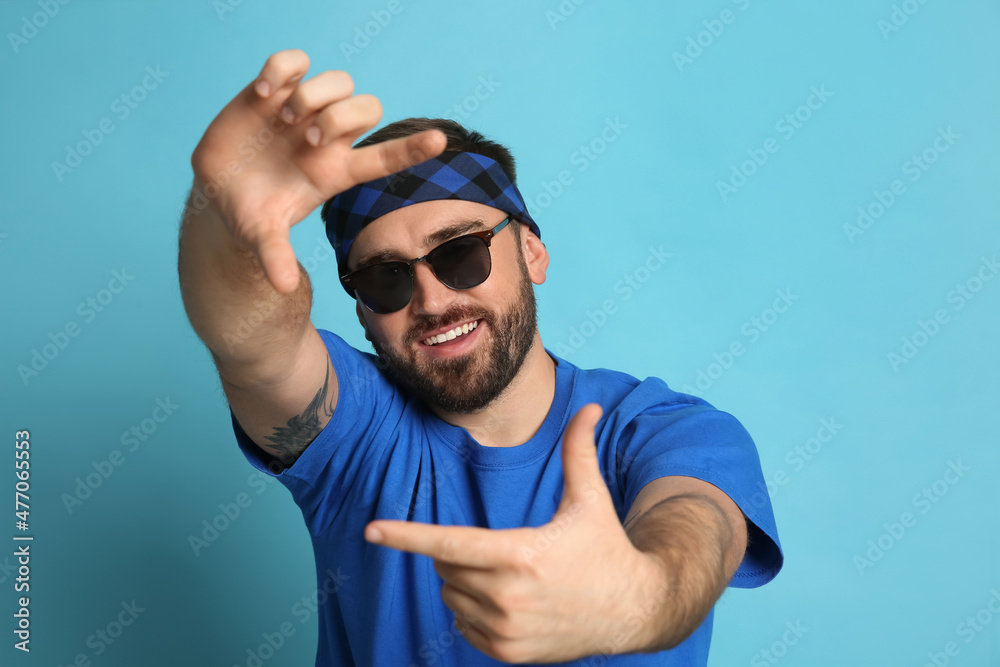 Naklejka premium Fashionable young man in stylish outfit with bandana on light blue background