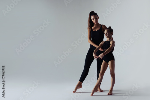 Gymnastic coach helping little girl to do exercise on white background