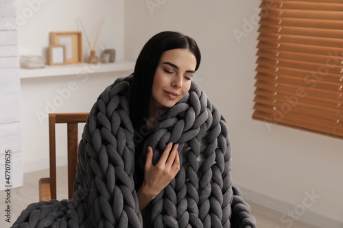 Young woman with chunky knit blanket in armchair at home