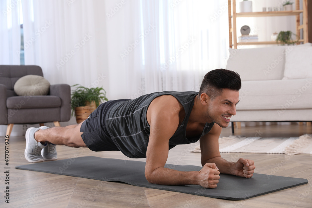 Handsome man doing plank exercise on yoga mat at home - obrazy, fototapety, plakaty 