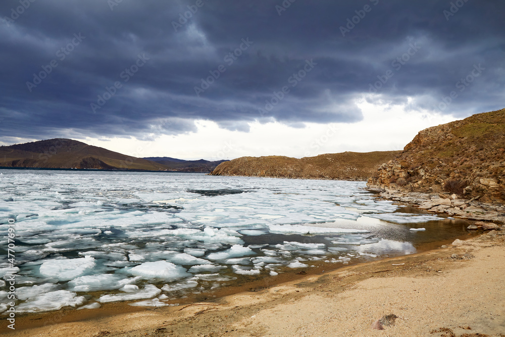 Spring landscape of Lake Baikal on a cloudy day. Ice drift, large ice floes floating in the lake. The shore of the lake near the island of Olkhon. Spring landscape of Lake Baikal on a cloudy day. Ice drift, large ice floes floating in the lake. The shore of the lake near the island of Olkhon.