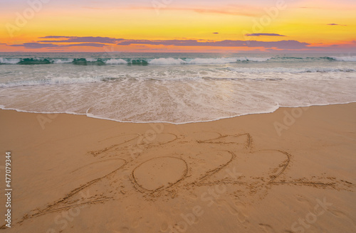 Fototapeta Naklejka Na Ścianę i Meble -  Happy New Year 2022, Lettering on the beach with waves and sunset sky Numbers 2022 year on the seashore, Message hand written in the golden sand on beautiful sunset or sunrise golden sky background